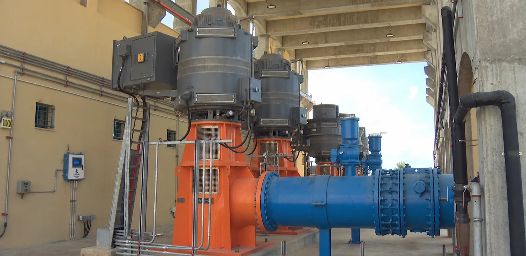 Water-treatment pumping hall with orange pumps, blue pipework and a Lexaloop WaterQ Basic analyzer digitally added to the left wall